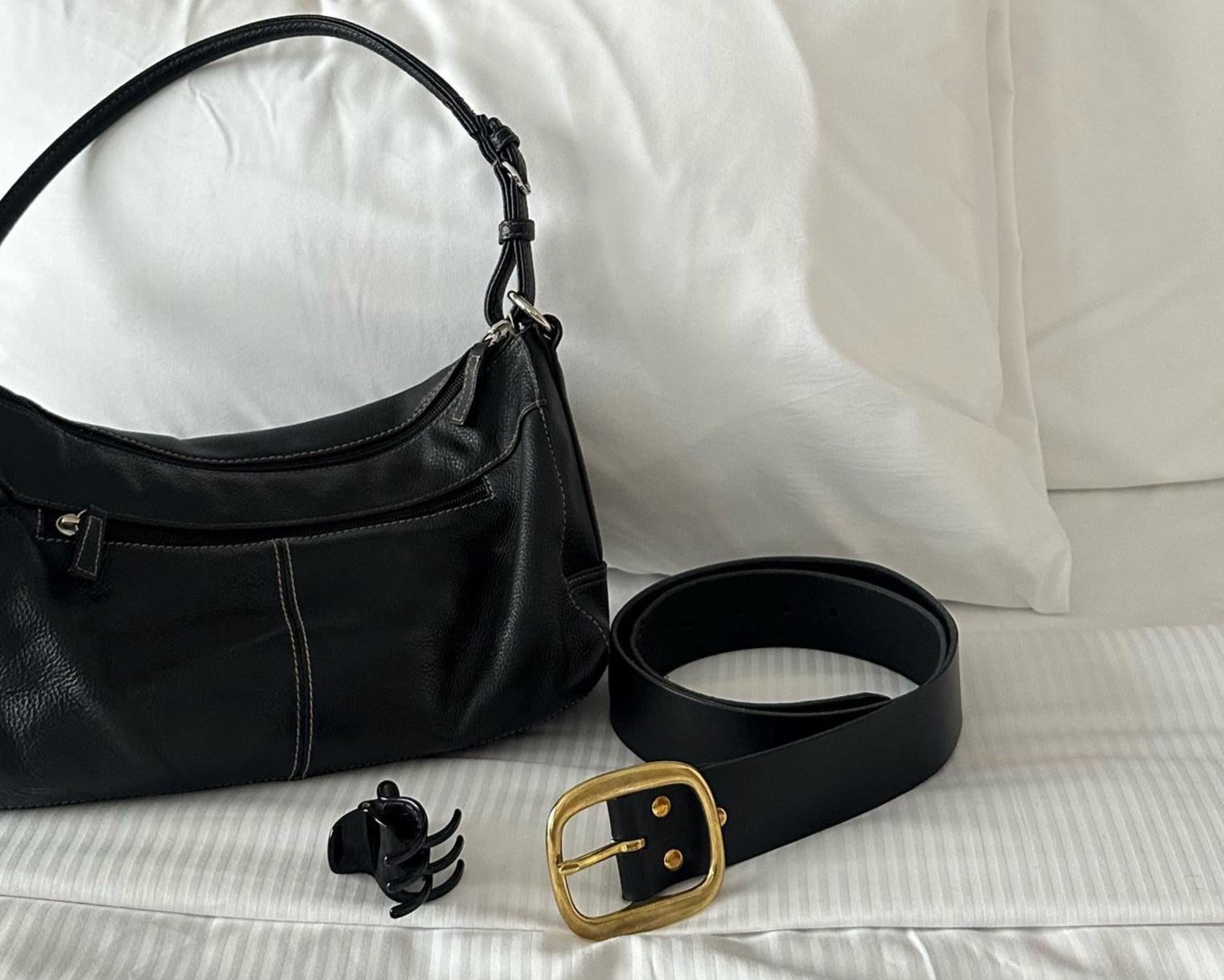 Black handbag and belt on a white bed
