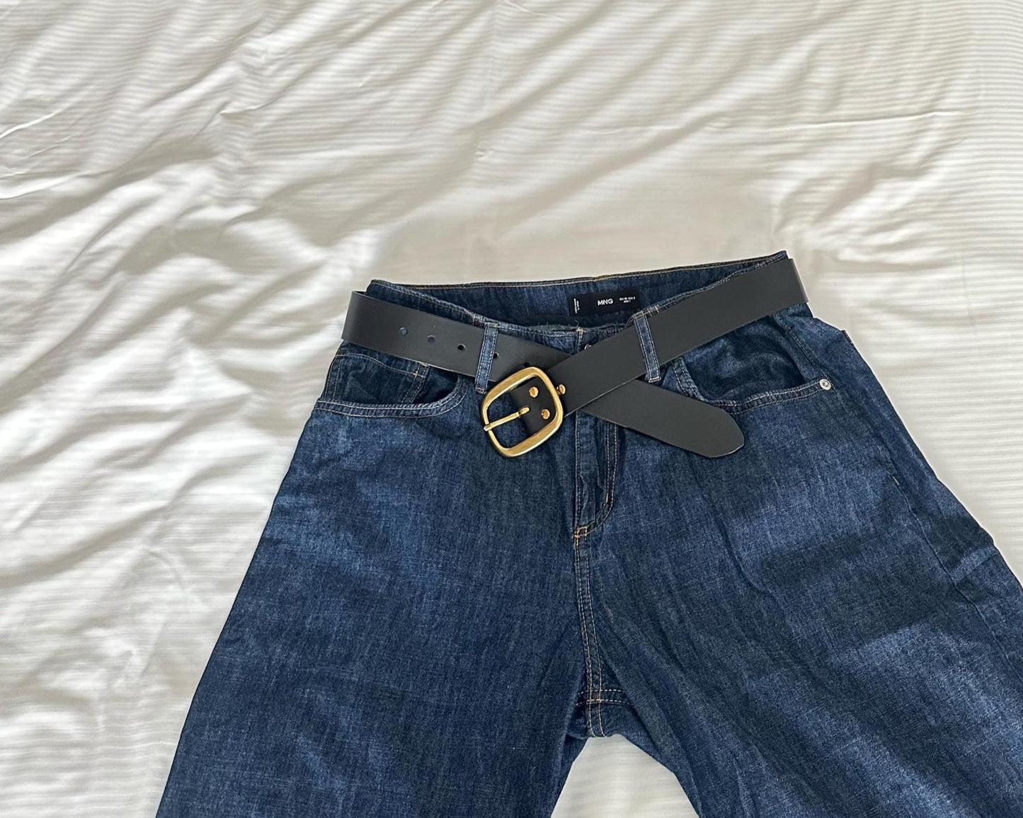 Blue jeans with a black belt and gold buckle on a white background