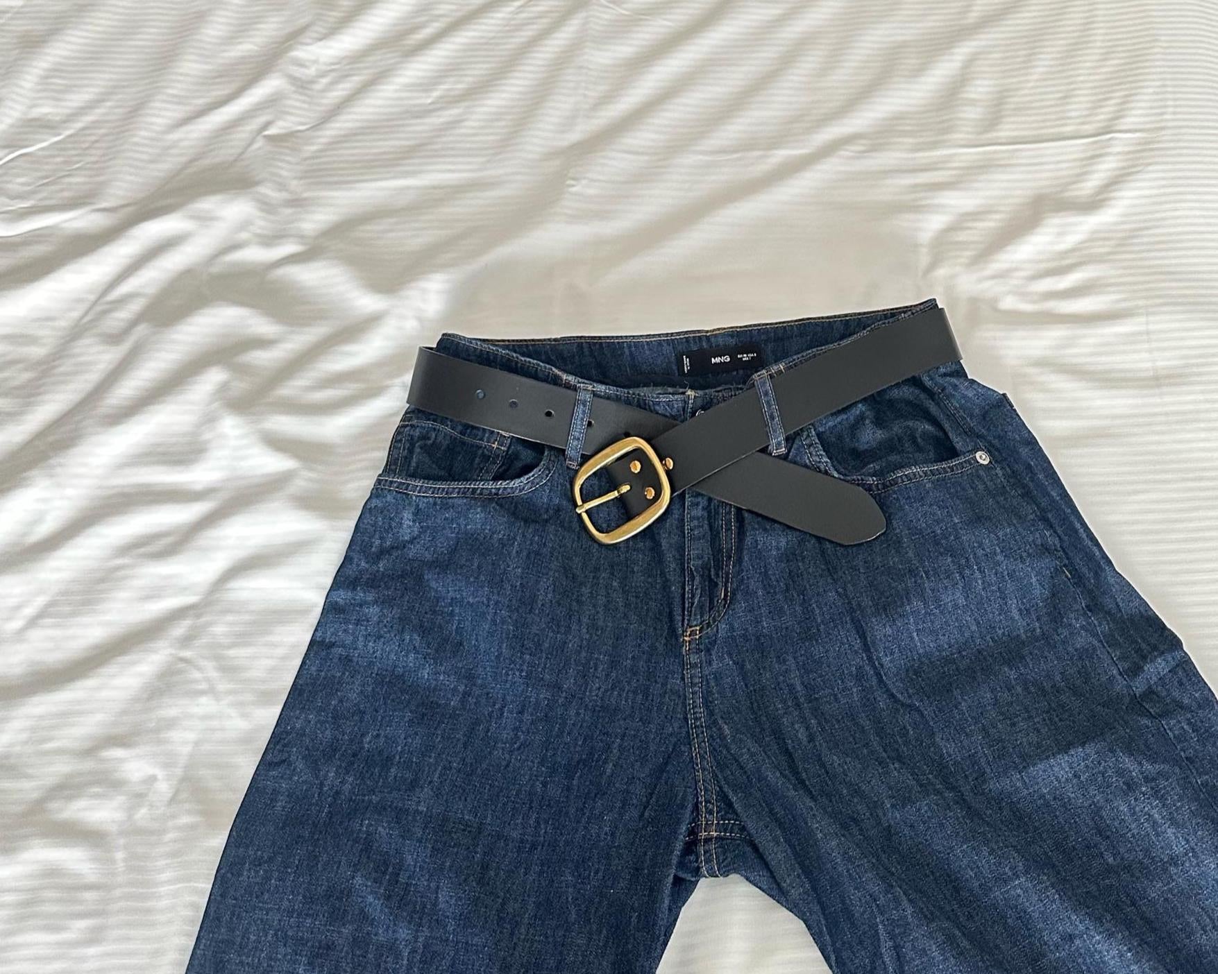 Blue jeans with a black belt and gold buckle on a white background
