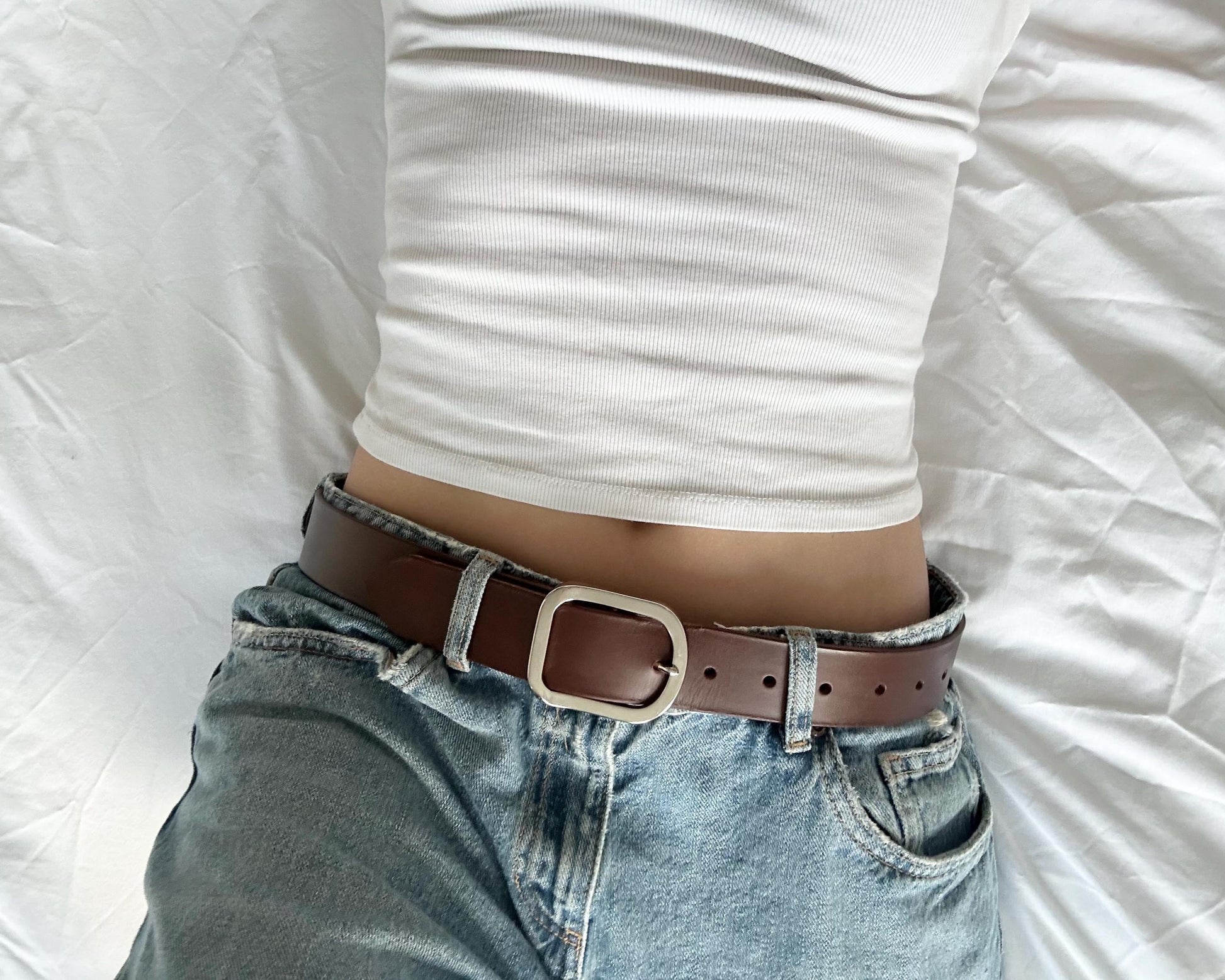 Person wearing a brown belt with a silver buckle on a white background