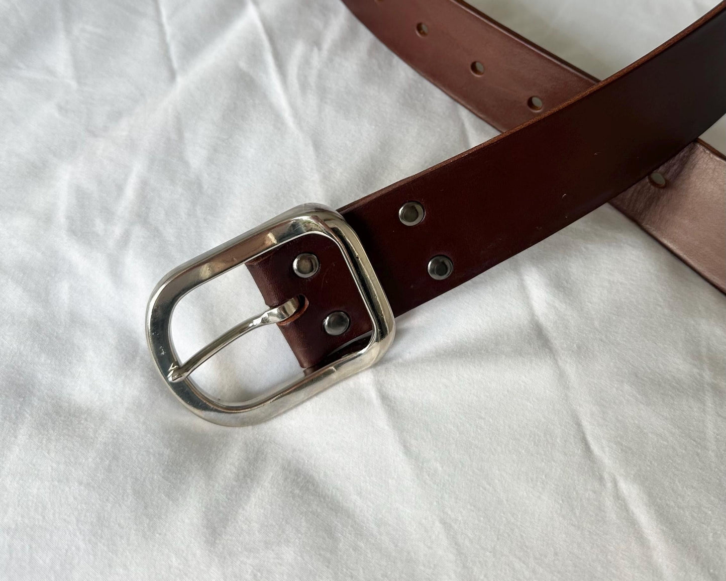 Brown leather belt with silver buckle on a white fabric background