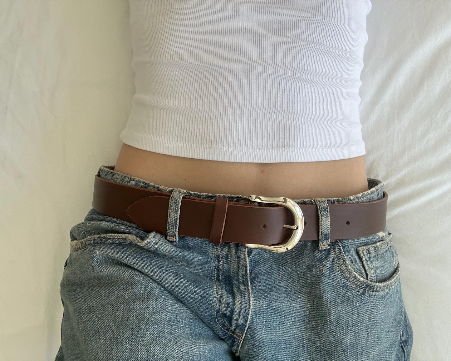 Person wearing a brown belt with a silver buckle on blue jeans against a neutral background