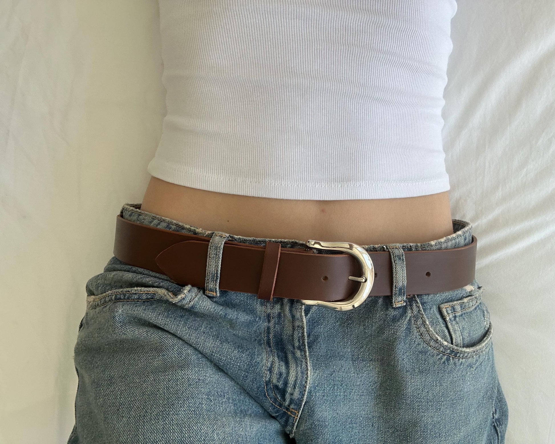 Person wearing a brown belt with a silver buckle on blue jeans against a neutral background